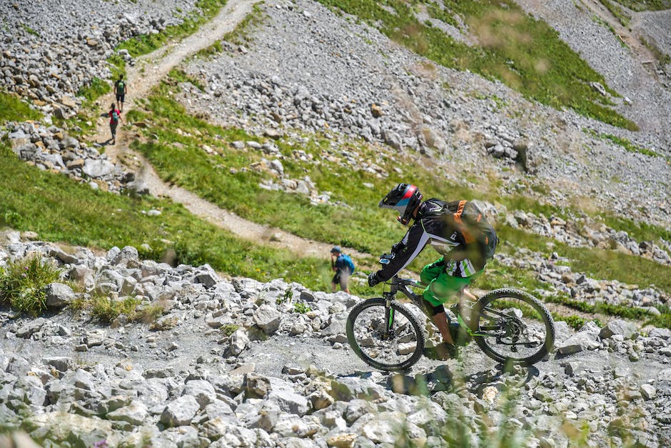 A person on a bike is riding up and over a rocky trail with mountains in the background.