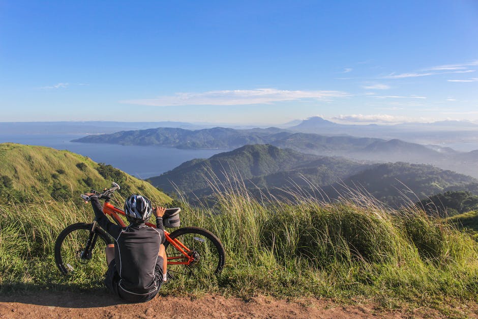 A person riding a mountain bike along a rocky, intermediate-level trail with a beautiful mountain view in the background.