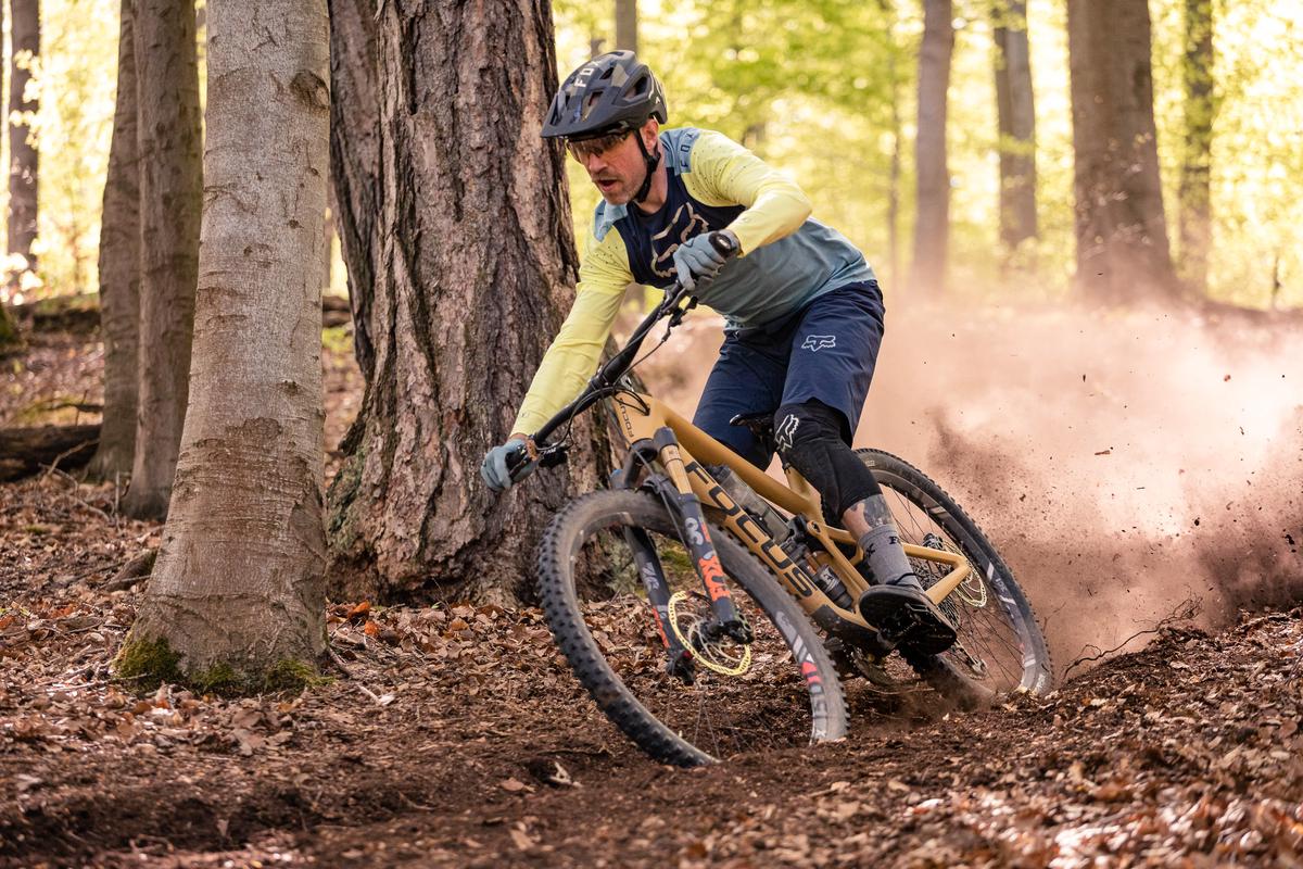A picture of a mountain biker riding on Strand Hill Trail with a view of the beautiful meadow and mountain slopes in the background.