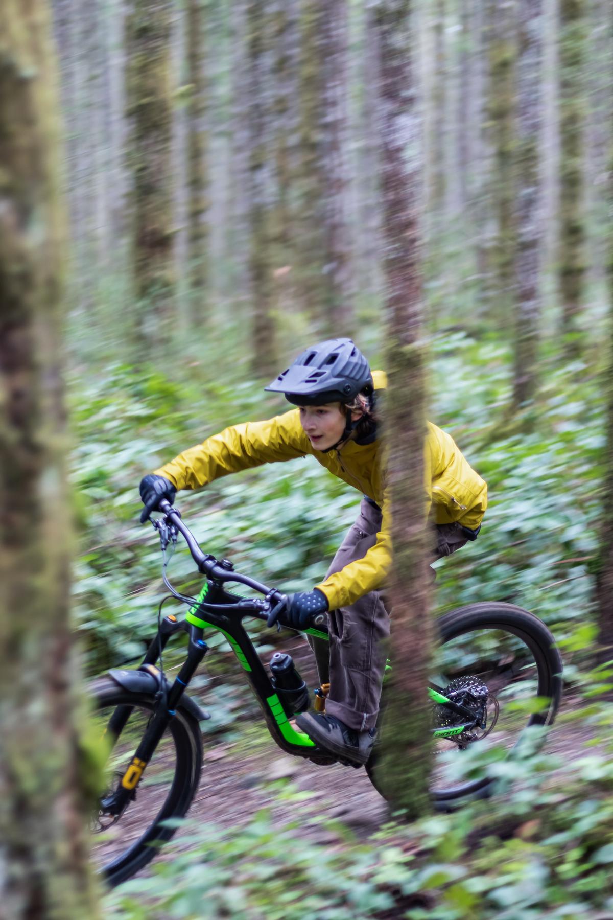 A person wearing a helmet and protective gear while riding a mountain bike on a trail surrounded by mountains and trees.